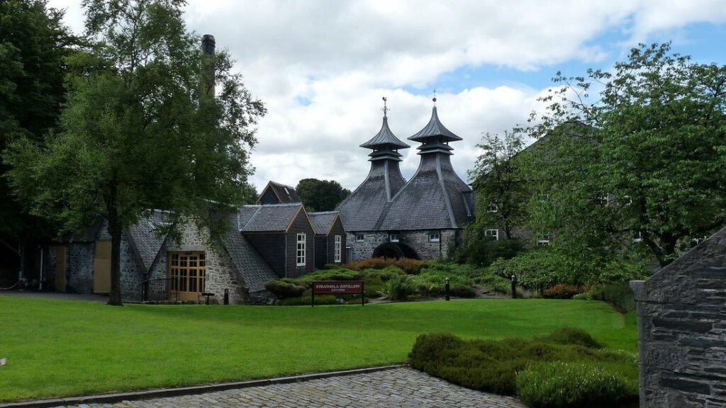 Bâtiments de pierre d'une distillerie coiffés de toits en pagode, autour d'une pelouse verte