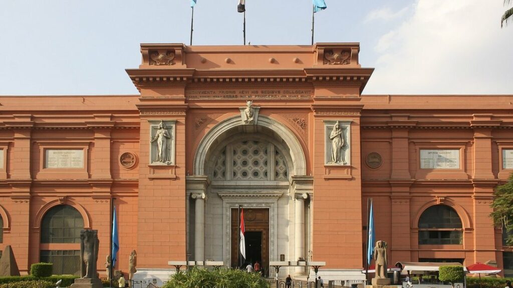Façade en brique rouge du musée égyptien, avec son porche central et ses statues sculptées