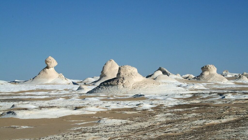 Rochers de craie blancs aux formes arrondies sur un sol de sable clair, sous un ciel bleu