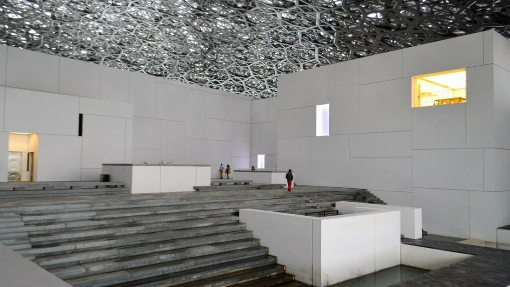 Sous le dôme ajouré du Louvre Abu Dhabi, des volumes blancs et des gradins de pierre grise