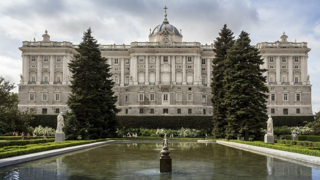 Façade du Palais royal de Madrid derrière un bassin, des pelouses taillées et deux grands conifères