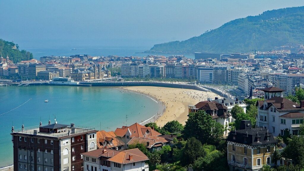 Vue d'ensemble de la plage de La Concha à Saint-Sébastien, entre l'eau turquoise, les immeubles et une colline verte
