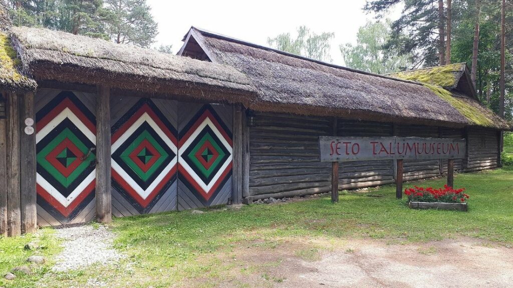 Grange en bois au toit de chaume, portes peintes de grands losanges verts, rouges et blancs