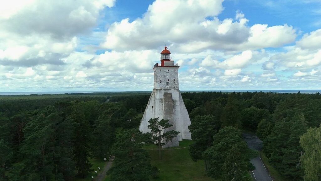 Phare blanc de Kõpu émergeant d'une forêt dense, vu du ciel, avec des nuages au-dessus