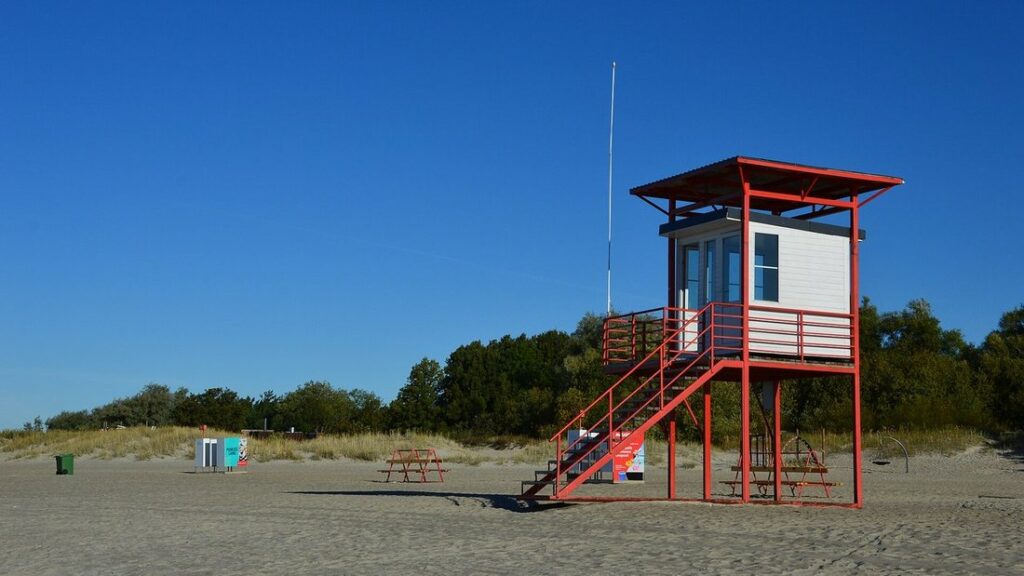 Tour de surveillance rouge et blanche sur une plage de sable, sous un grand ciel bleu