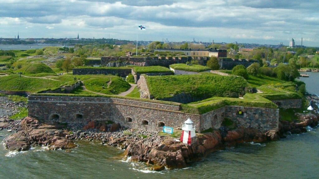 Remparts de pierre et pelouses de la forteresse de Suomenlinna sur ses îlots, avec la mer et un petit phare rouge et blanc