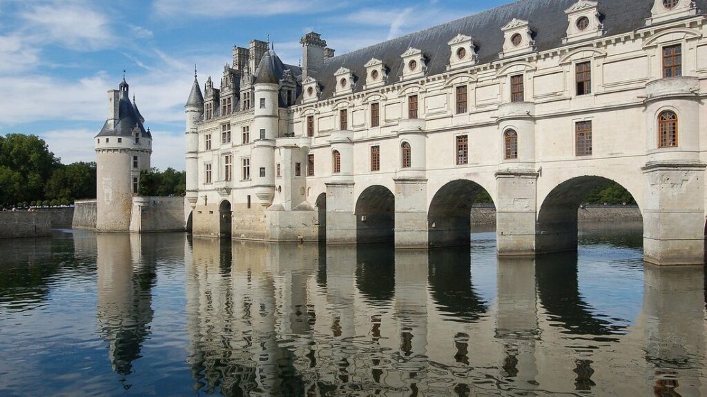 Château de pierre blanche posé sur des arches qui enjambent une rivière, avec son reflet dans l'eau