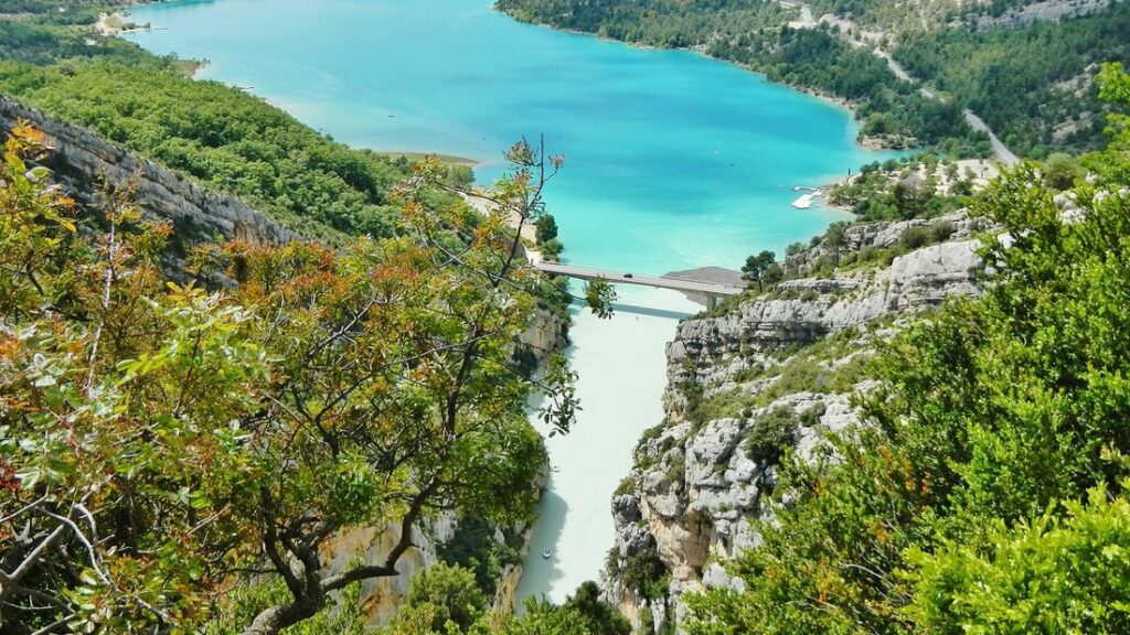 Eau turquoise d'un lac prolongeant un canyon de calcaire couvert de végétation, avec un pont au loin
