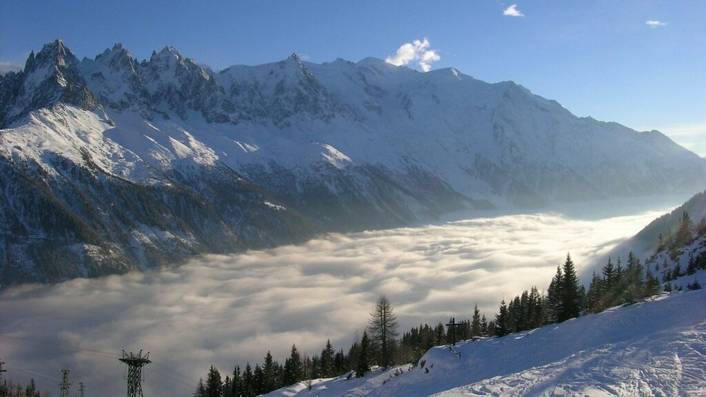 Chaîne de montagnes enneigées dominant une vallée remplie d'une mer de nuages