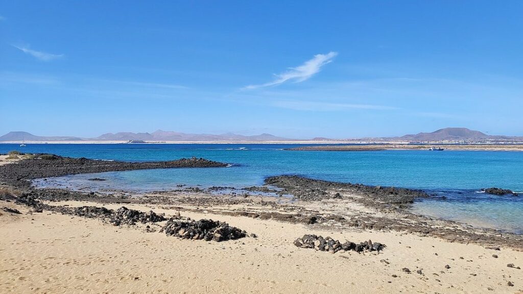 Plage de sable clair et rochers noirs au bord d'une eau turquoise, sur l'îlot de Lobos