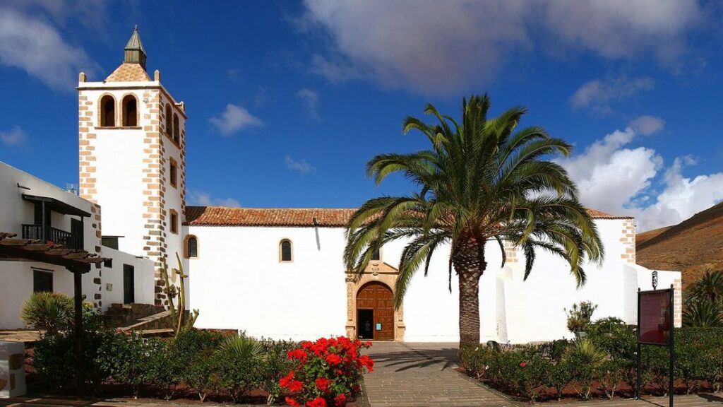 L'église blanche Santa María de Betancuria, avec son clocher et un palmier, sous un ciel bleu
