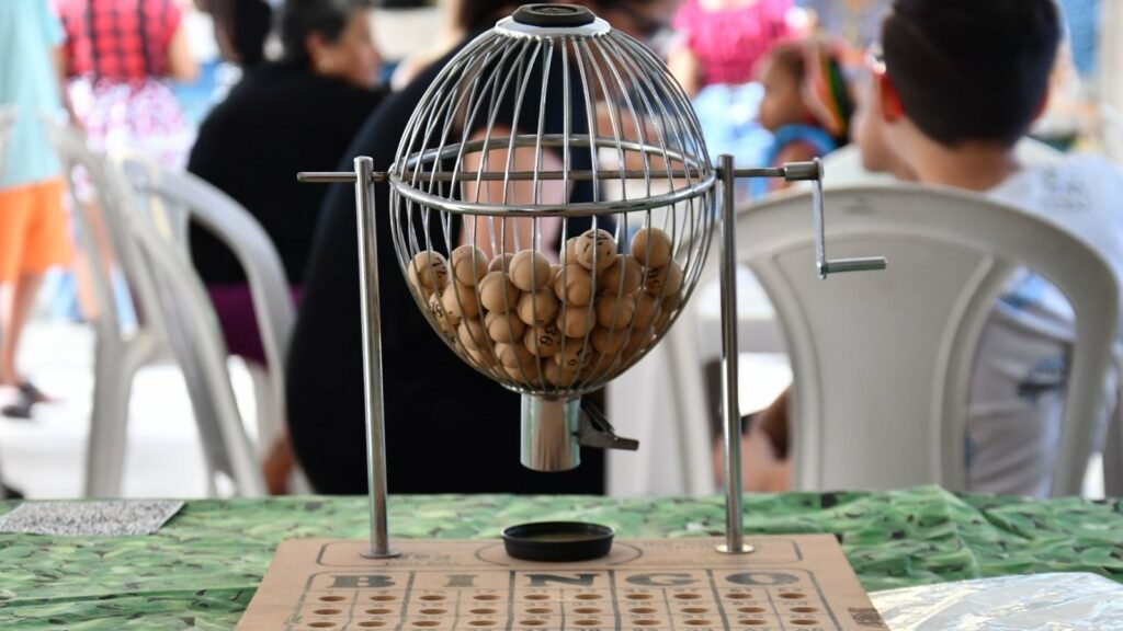 Tambour de tirage à boules numérotées en bois posé sur un plateau de bingo, public flou à l'arrière-plan