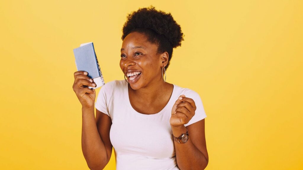 Femme rieuse tenant un petit carnet bleu devant un fond jaune uni