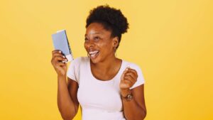 Femme rieuse tenant un petit carnet bleu devant un fond jaune uni