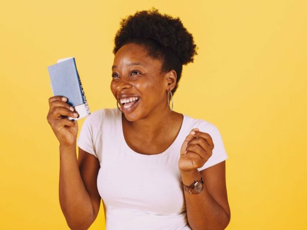 Femme rieuse tenant un petit carnet bleu devant un fond jaune uni
