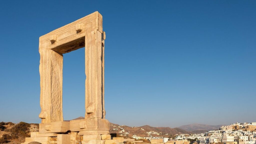 Grande porte de marbre blanc de la Portara contre un ciel bleu, avec les maisons blanches de Naxos en contrebas