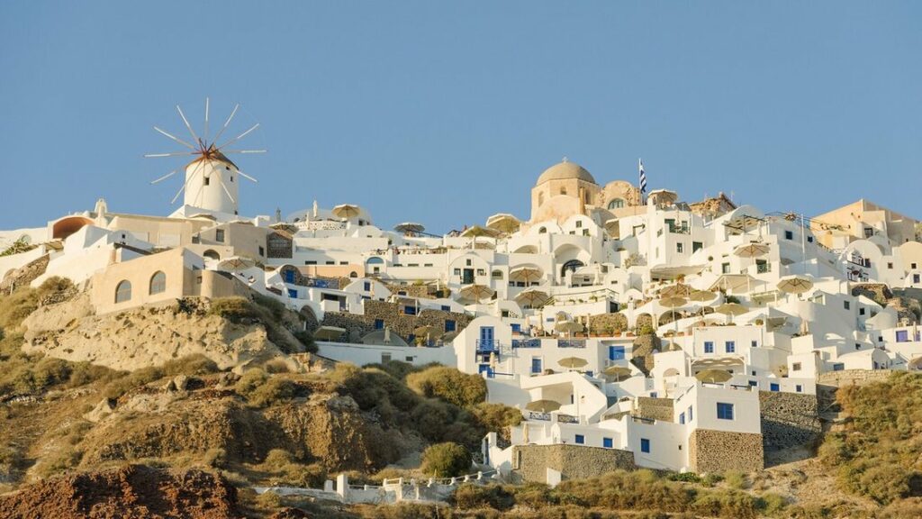 Maisons blanches et dômes d'églises d'Oia serrés sur la falaise de Santorin, avec un moulin à vent