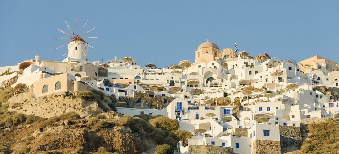 Maisons blanches et dômes d'églises d'Oia serrés sur la falaise de Santorin, avec un moulin à vent