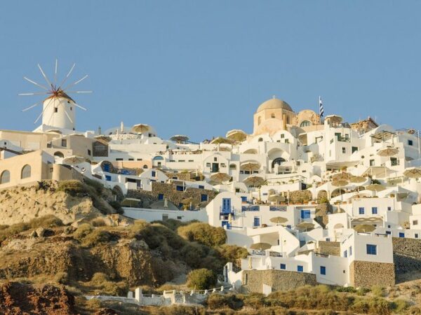 Maisons blanches et dômes d'églises d'Oia serrés sur la falaise de Santorin, avec un moulin à vent