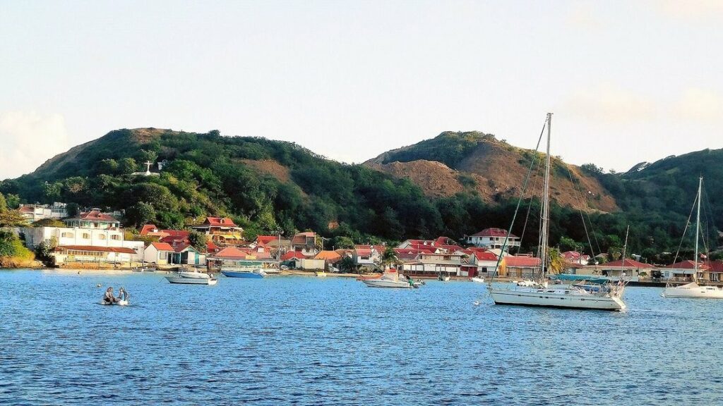 Maisons aux toits rouges le long de la baie de Terre-de-Haut, avec un voilier et des collines vertes