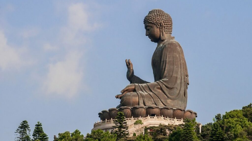 Statue géante en bronze du Tian Tan Buddha, assise sur un socle de lotus, vue de profil au-dessus des pins