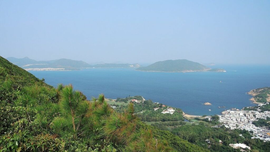 Vue depuis la crête sur la mer et des îles au loin, avec des pins au premier plan et des maisons en bord de mer