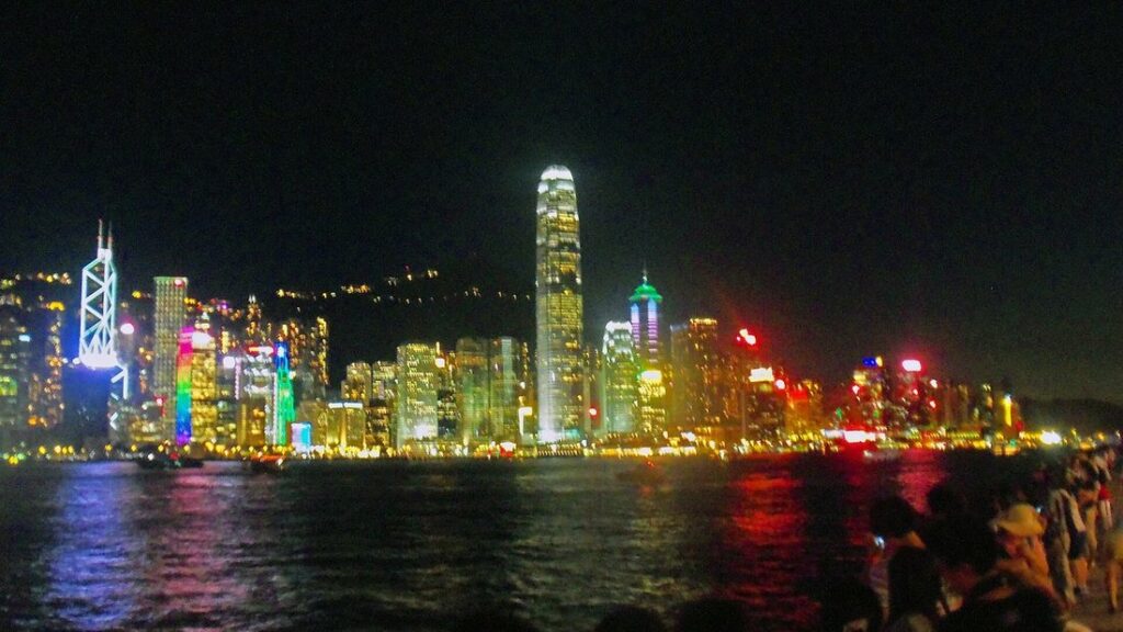 Gratte-ciel illuminés de Hong Kong Island reflétés dans l'eau du port la nuit, avec des spectateurs à droite