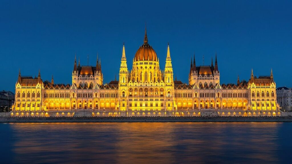 Le Parlement néo-gothique éclairé en jaune au bord du Danube, sous un ciel bleu sombre