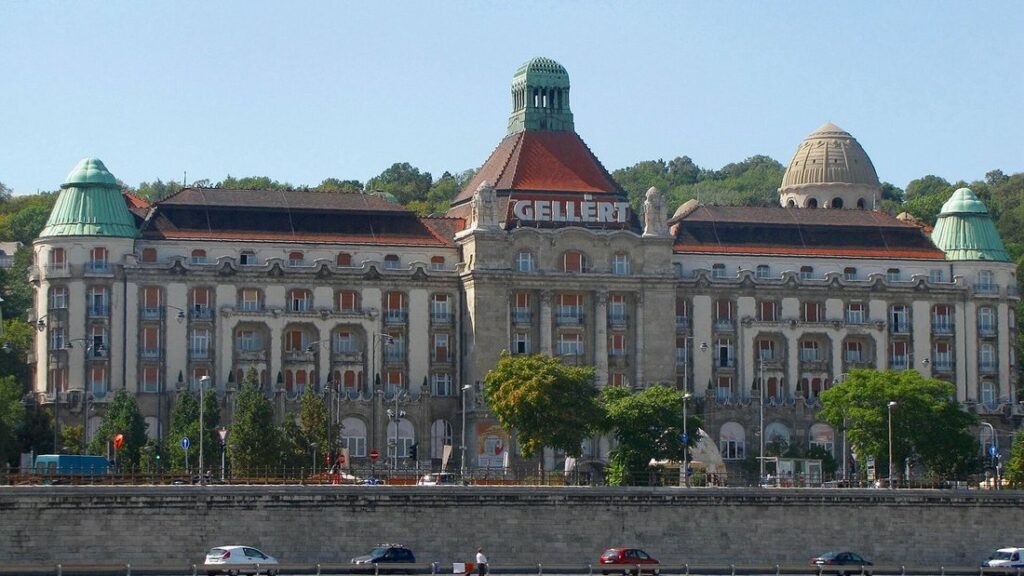 Façade Art nouveau de l'établissement de bains, avec ses coupoles vertes, derrière des arbres et une route