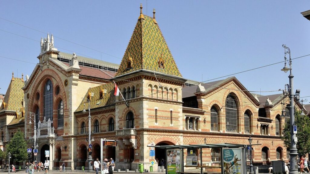 Façade en briques et tuiles colorées d'une grande halle de marché, avec un pignon central et un portail