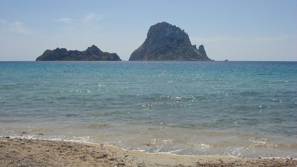 L'îlot rocheux d'Es Vedrà et ses voisins, vus depuis la plage de Cala d'Hort, sur une mer calme