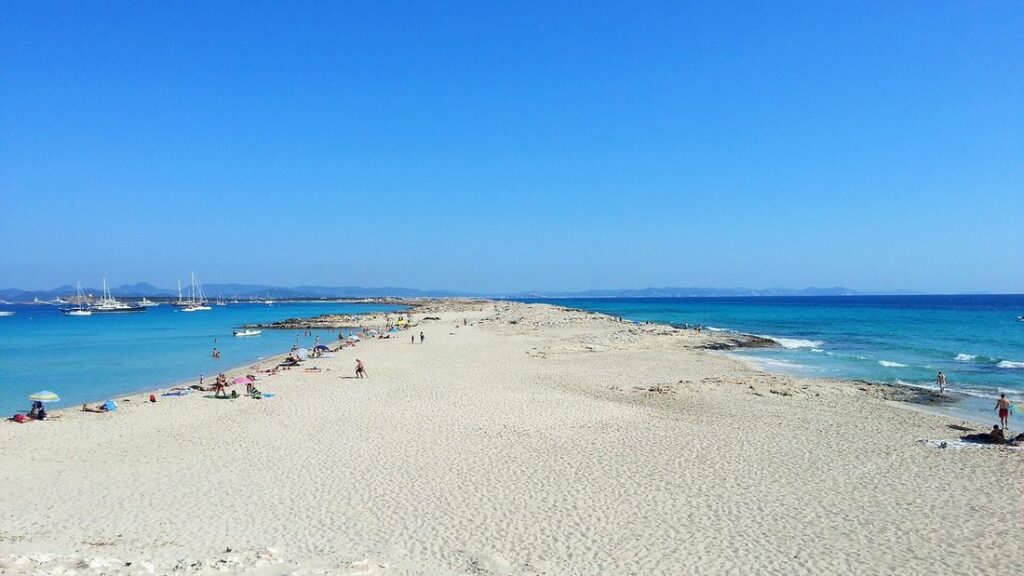 Longue langue de sable clair entre deux eaux turquoise à Ses Illetes, avec des voiliers au large