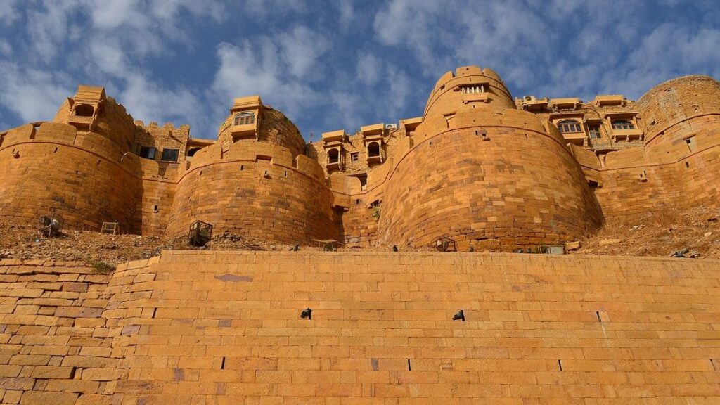 Bastions arrondis en pierre ocre du fort de Jaisalmer sous un ciel bleu nuageux