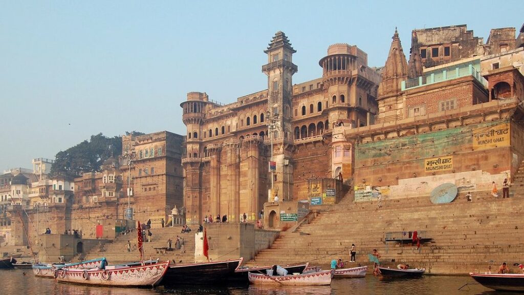 Ghats de Varanasi : bâtiments ocre et rouges dominant les marches, avec des barques amarrées sur le Gange