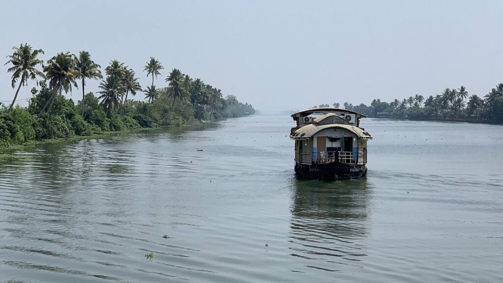 Un houseboat traditionnel avance sur un large canal bordé de cocotiers, près d'Alleppey