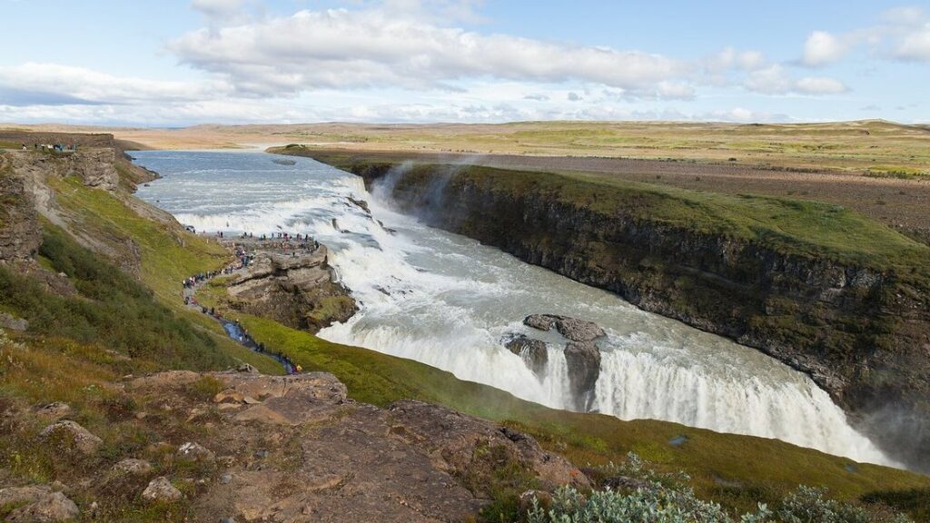 Rivière qui plonge en gradins dans un canyon aux parois sombres, sous un ciel partiellement nuageux