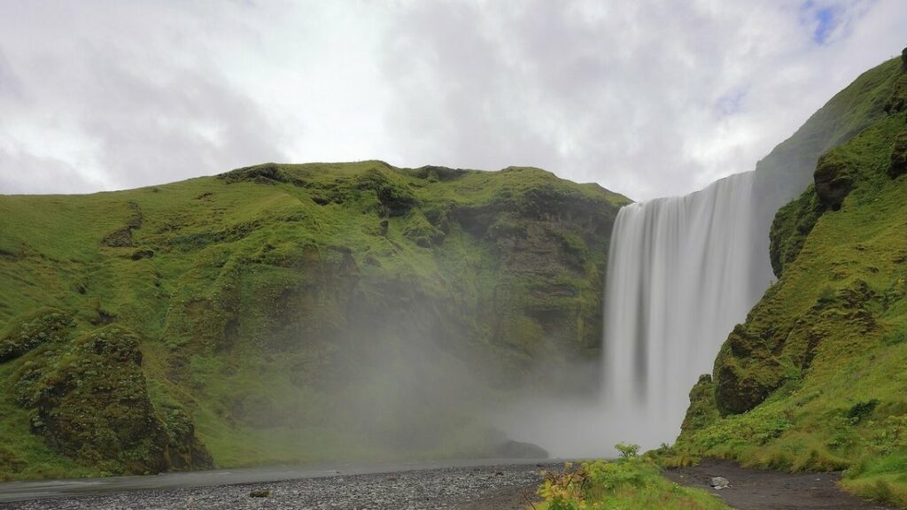 Haute cascade tombant d'une falaise verte, avec une brume d'eau à sa base