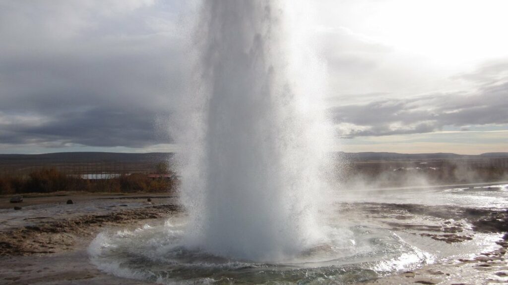 Jet d'eau et de vapeur qui jaillit d'un geyser, au-dessus d'un bassin entouré de terre brune