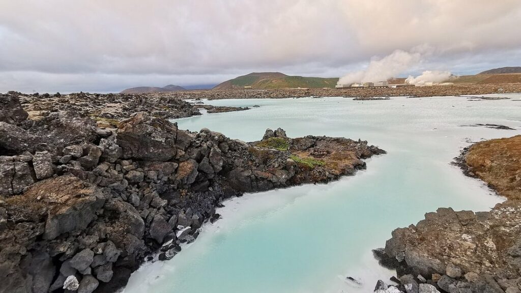 Eau laiteuse d'un bleu turquoise entre des roches de lave sombres, avec de la vapeur au loin