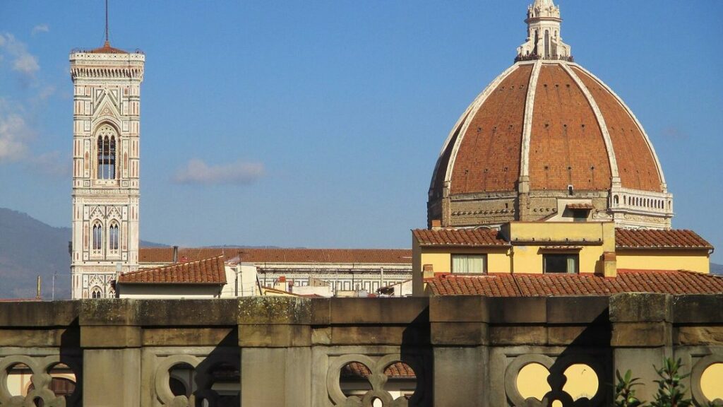 Dôme de brique rouge de la cathédrale de Florence et campanile clair, vus au-dessus des toits sous un ciel bleu