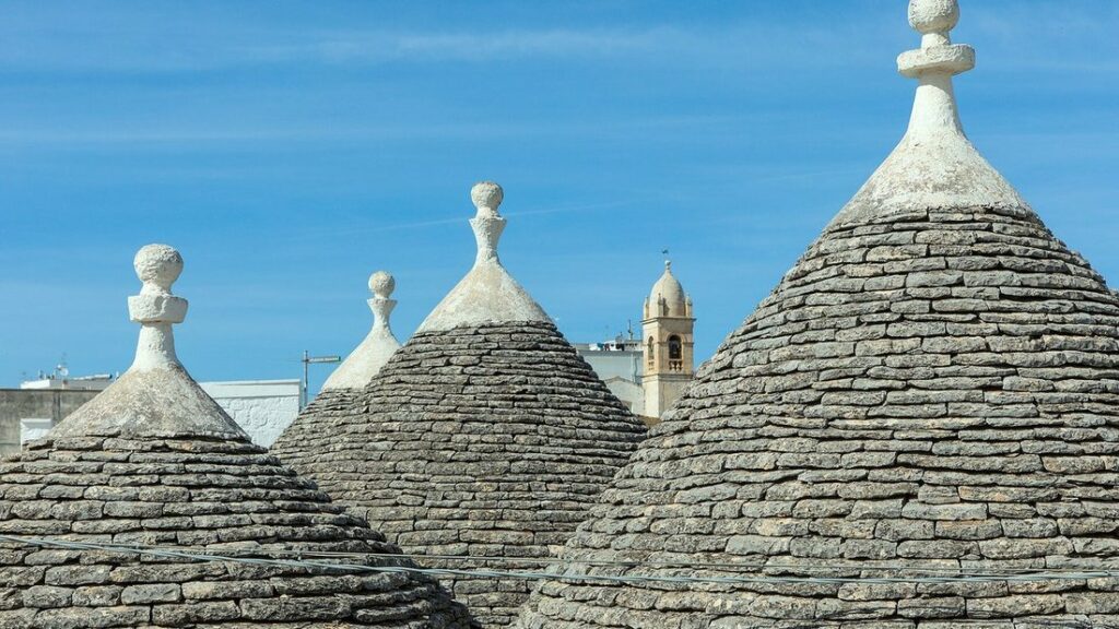 Toits coniques en pierre grise des trulli, surmontés de pinacles blancs, sous un ciel bleu