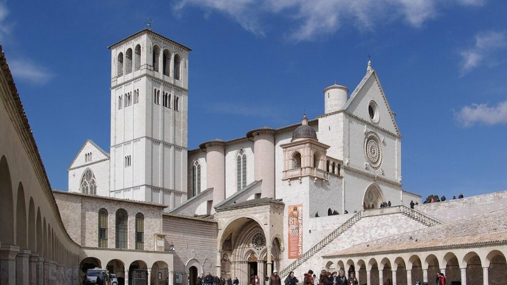 Basilique Saint-François d'Assise avec son haut campanile et ses arcades, sous un ciel bleu nuageux