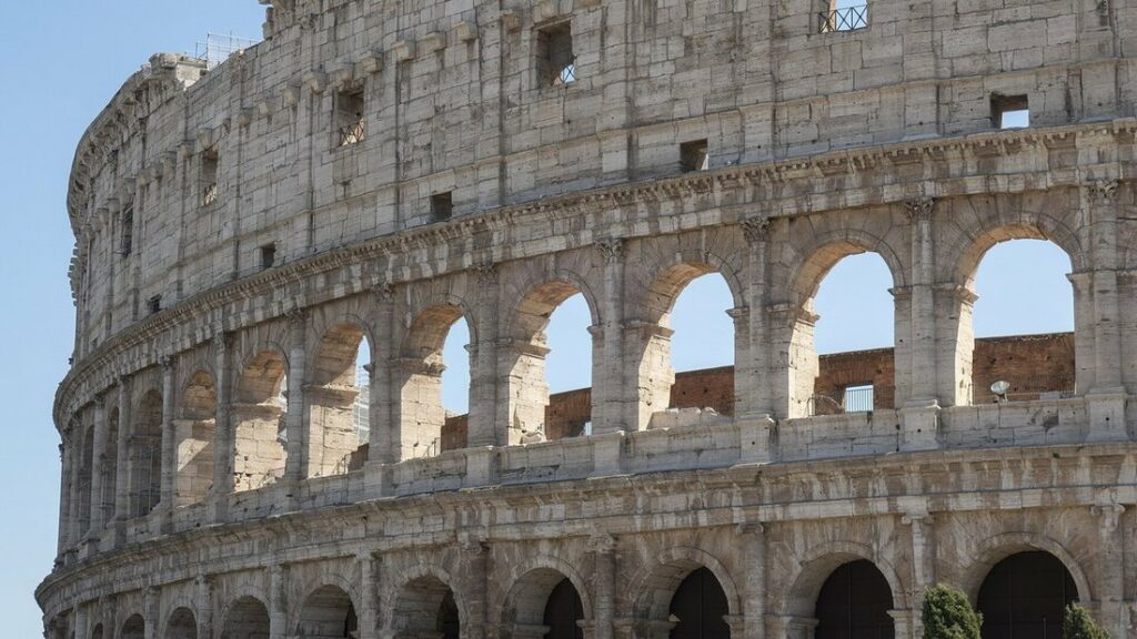 Façade extérieure en pierre du Colisée de Rome, avec ses arcades superposées sous un ciel nuageux