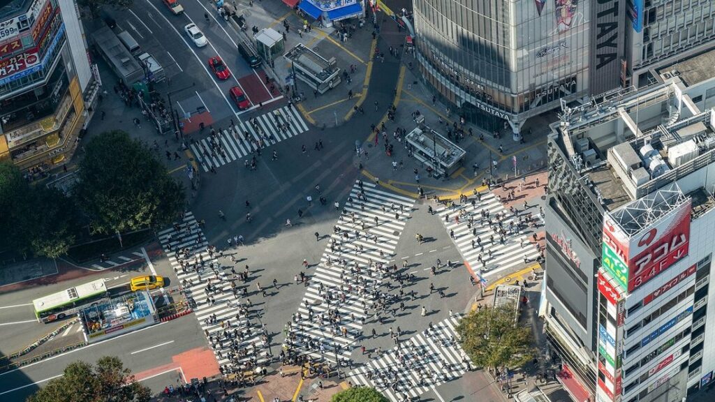 Vue plongeante sur le carrefour de Shibuya à Tokyo, ses passages piétons qui se croisent et les immeubles voisins