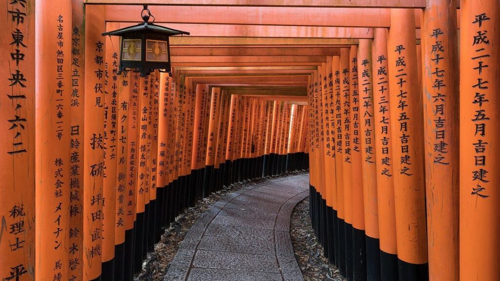 Tunnel de portiques torii orange vif au sanctuaire Fushimi Inari, avec une lanterne suspendue et un chemin dallé