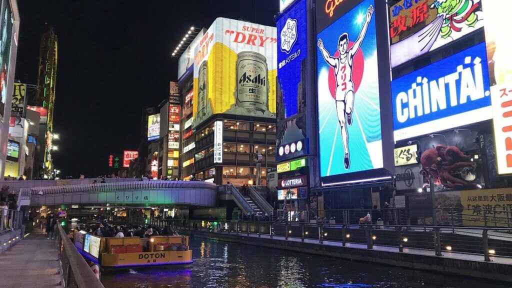 Enseignes lumineuses de Dotonbori à la tombée de la nuit, avec le canal et un bateau au premier plan