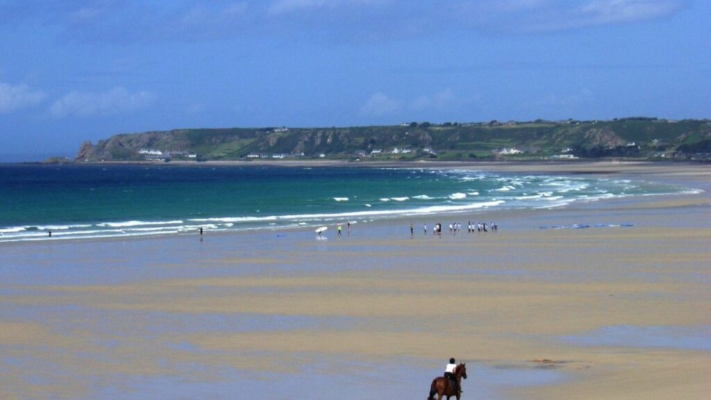 Longue plage de sable plate avec des vagues, des promeneurs au loin et un cavalier au premier plan