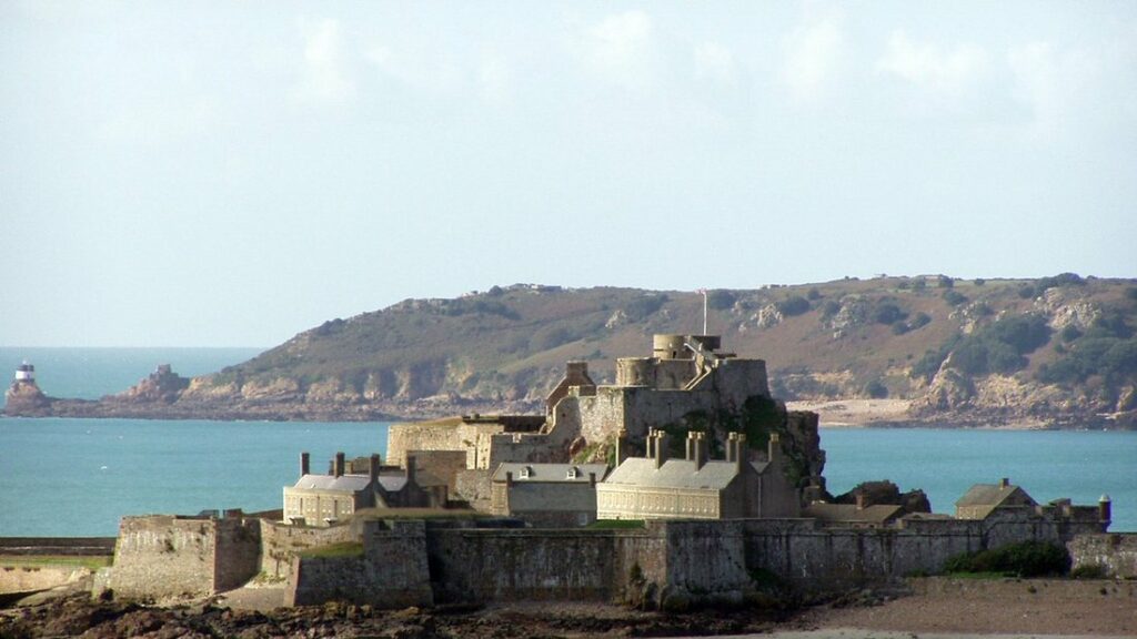 Forteresse de pierre sur un îlot rocheux face à la mer, avec la côte de Jersey en arrière-plan