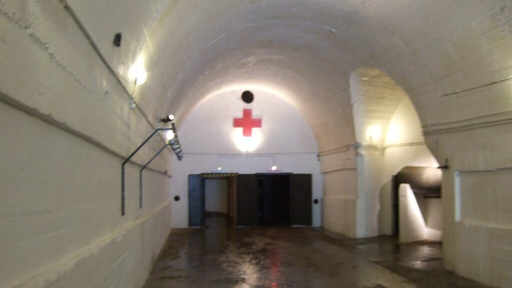 Couloir voûté d'un tunnel souterrain avec une croix rouge peinte au fond, au-dessus d'une porte