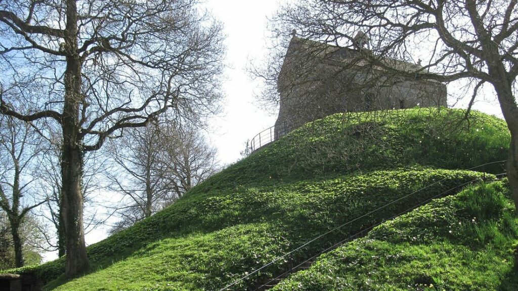 Tumulus herbeux dans un cadre d'arbres, surmonté d'une petite chapelle en pierre